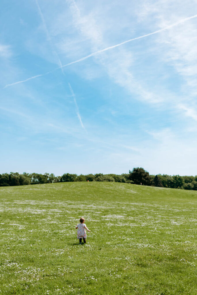 Kleines Mädchen läuft in Richtung Grashügel bei strahlend blauem Himmel.