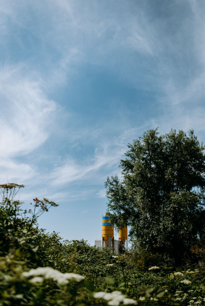 Gelbe und blaue Silos hinter Bäumen und Sträuchern vor blauem Himmel in Stellendam