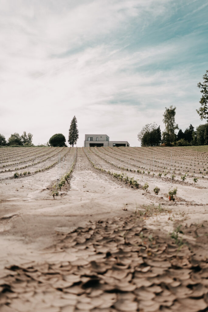 Ackerlandschaft mit trockenem Boden im Vordergrund und einem einzelnen Haus in der Ferne.