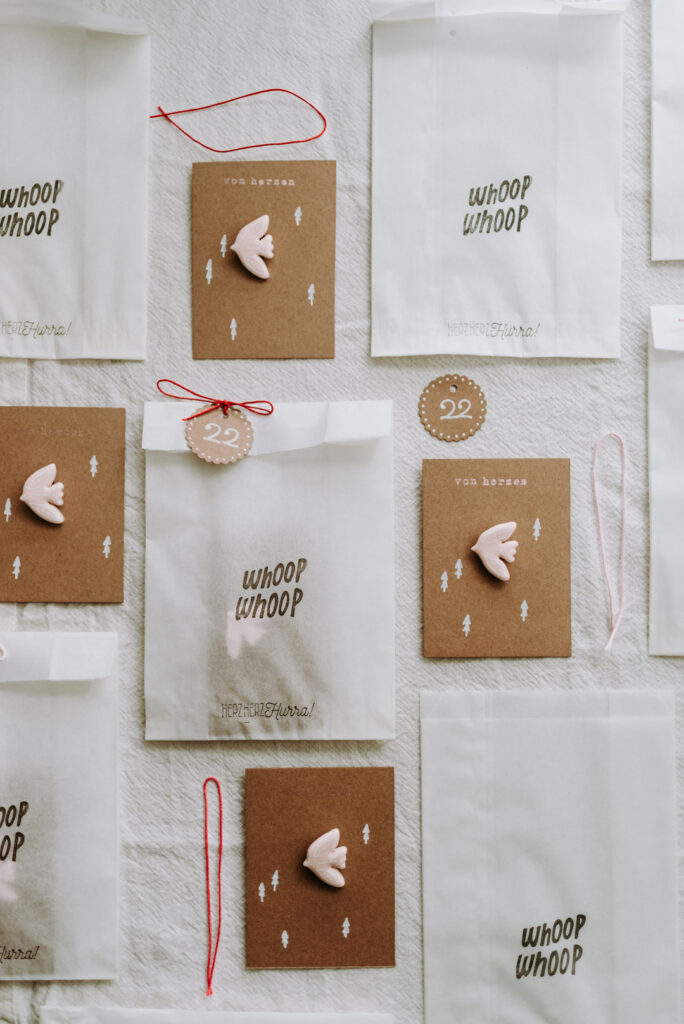 Übersicht aus Karten mit roséfarbenen Vogel-Ansteckern aus Clay (Polymer Clay), weißen Geschenktüten, Schnüren und Anhängern mit der Zahl 22.