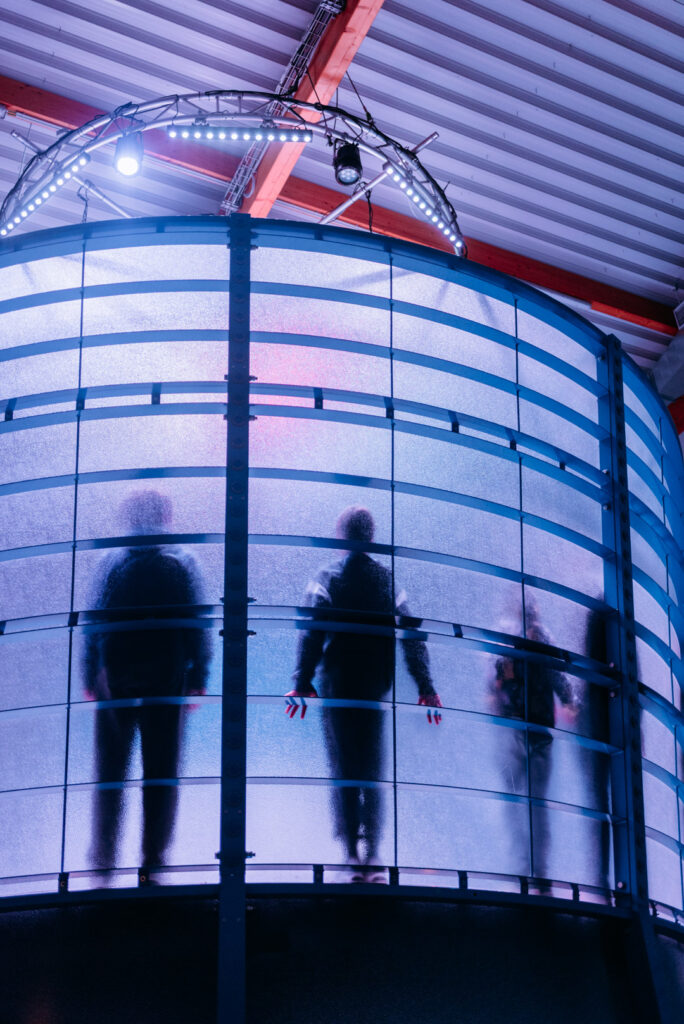 Mehrere Personen als dunkle Silhouetten hinter einer blauen Glasfassade.