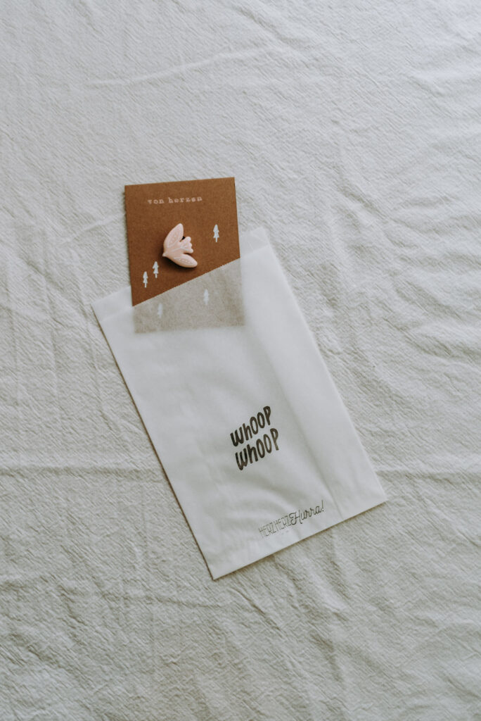 Weiße Geschenktüte mit der Aufschrift „whoop whoop“, kombiniert mit einer „von herzen“-Karte und einem Vogel-Anstecker aus Clay (Polymer Clay).