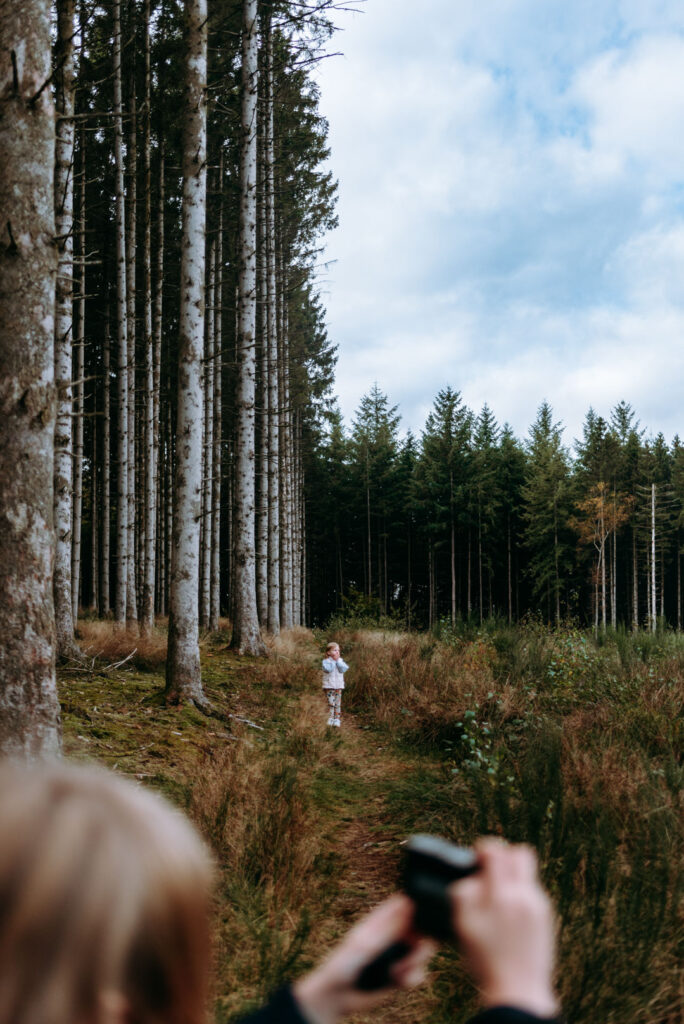 Kind steht auf einem Waldweg und ein weiteres im Vordergrund, das fotografiert.