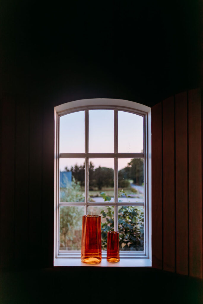 Fenster mit zwei orangefarbenen Glasvasen im Abendlicht.