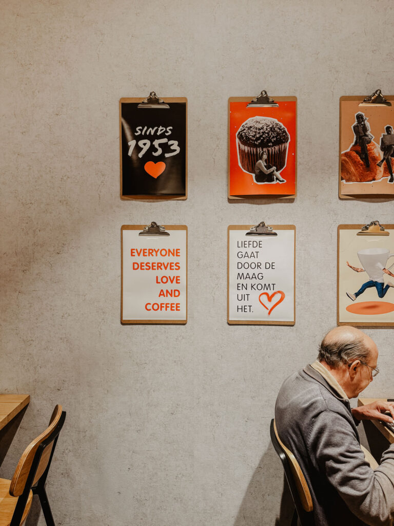 Älterer Mann sitzt vor einer Wand mit Kaffee-Schriftzügen und Zitaten.