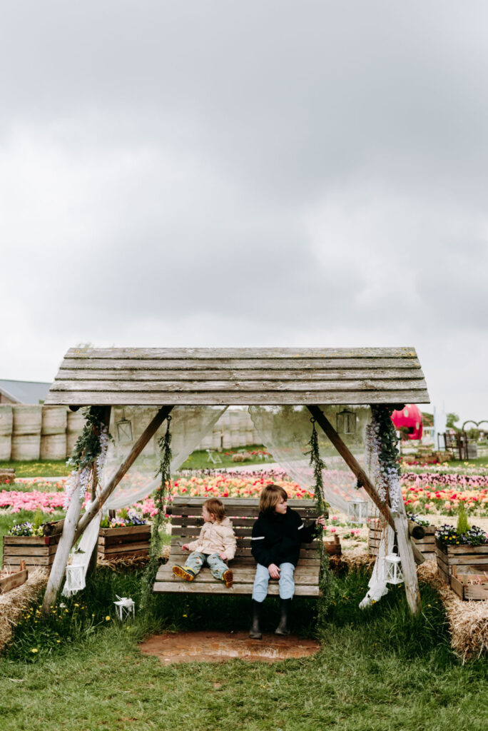 Zwei Kinder auf einer Holzschaukel vor Tulpenfeldern auf dem Krewelshof