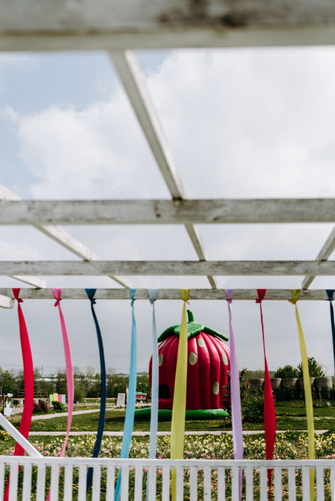 Bunte Bänder an einer Pergola mit Erdbeer-Hüpfburg im Hintergrund