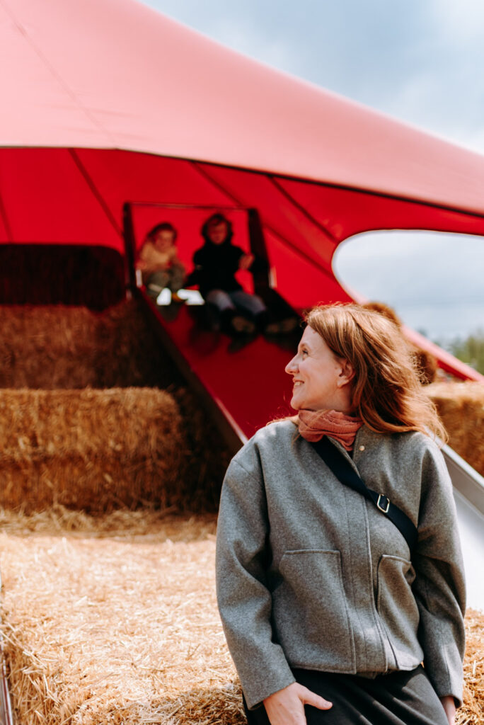 Frau vor einer großen Rutsche aus Strohballen unter einem roten Zelt